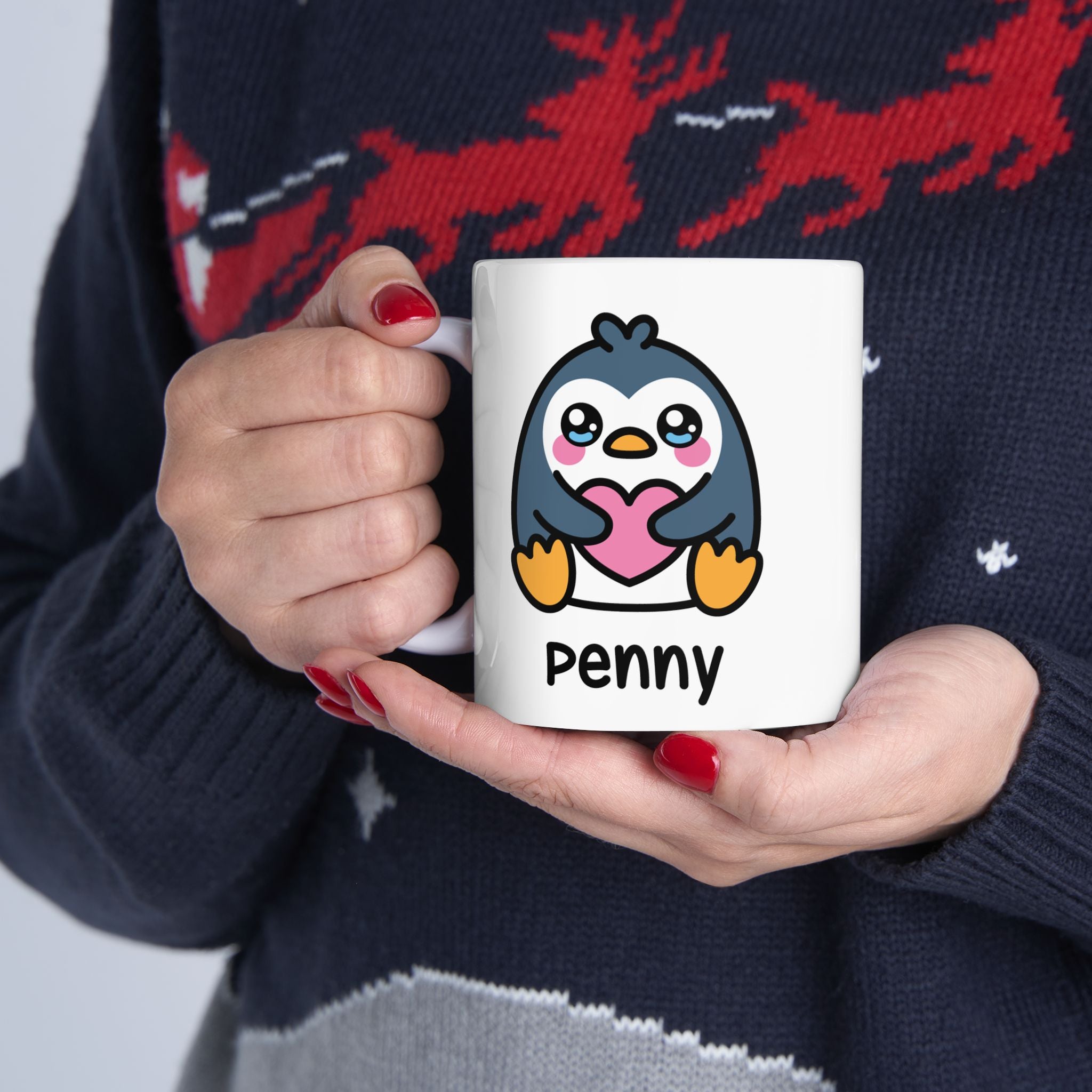 Person holding a mug with a penguin design, wearing a dark sweater with red reindeer pattern.