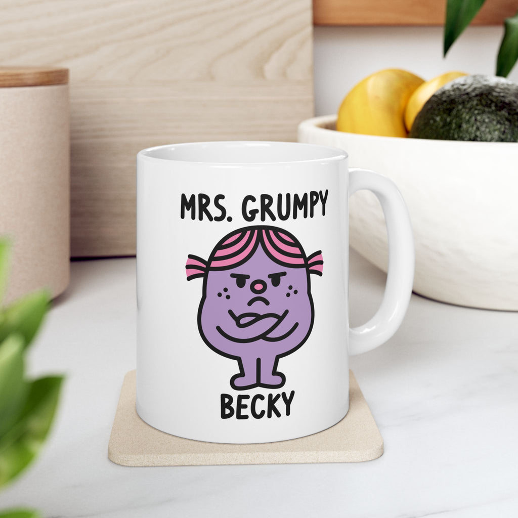 White mug with cartoon character and text 'Mrs. Grumpy' on a wooden coaster.
